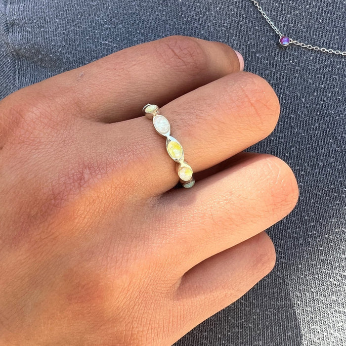 A hand holding a silver Eternity ring with a white and yellowish stone inlay