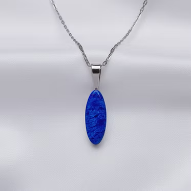 A silver chain necklace with an oval blue stone pendant, displayed against a white satin fabric background.