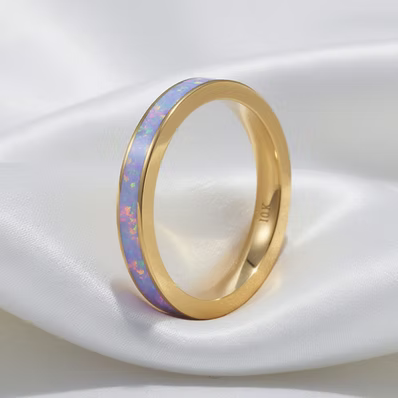 A gold band ring with a light blue iridescent inlay, resting on a draped white satin fabric.