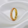 A gold band ring featuring a vibrant iridescent inlay of pink, orange, and blue opal, resting on a draped white satin fabric.