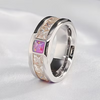 A silver-toned ring with a polished band, featuring a central square pink gemstone and clear crystal-like accents on a soft white fabric background.