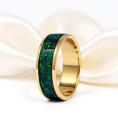A gold band ring featuring a textured green inlay, displayed on a soft white satin fabric background.