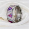 A polished silver-toned band ring featuring inlaid triangular opal segments in vibrant pink, purple, blue, and white, displayed on a draped white satin fabric.