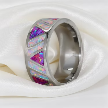 A polished silver-toned band ring featuring inlaid triangular opal segments in vibrant pink, purple, blue, and white, displayed on a draped white satin fabric.