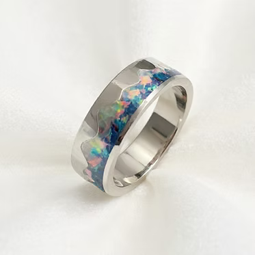 A polished silver band ring featuring a vibrant, multicolored inlay of opal with shades of blue, green, pink, and orange, set against a clean white background.