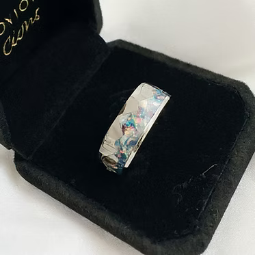 A silver-toned ring with a round clear gemstone set in a black square presentation box on a white background.