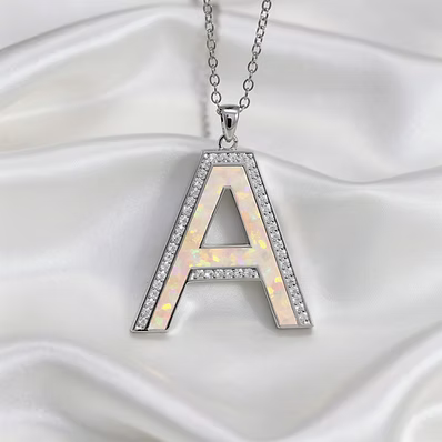 A silver letter 'A' pendant necklace with a white iridescent inlay and clear rhinestone accents, displayed on a draped white satin fabric background.