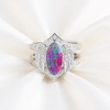 A silver ring featuring a large marquise-cut iridescent opal center stone with wing-like side details and small clear stones, displayed on a soft white fabric background.