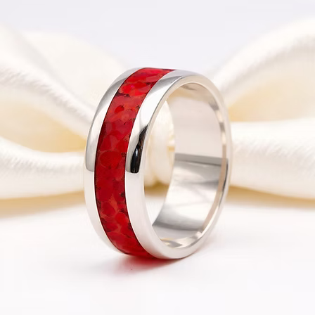 A polished silver band ring featuring a vibrant red textured inlay, displayed on a soft white satin ribbon.