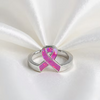 A silver ring featuring a pink opal inlaid awareness ribbon, displayed on a white satin fabric background.