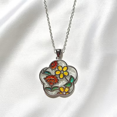 A silver-tone flower-shaped pendant necklace with colorful enamel floral details, displayed on a white satin fabric background.