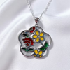 A silver-tone floral pendant necklace with colorful enamel details, featuring a yellow flower, red rose, and green leaves on a white satin background.