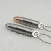 Two bullet-shaped pendant necklaces with engraved text, one in polished silver and one in rose gold, resting on a white textured surface.