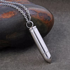 A silver bullet-shaped pendant necklace on a matching chain, displayed on a textured gray surface next to a dark polished stone.