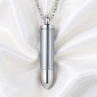 A silver bullet-shaped pendant necklace on a delicate silver chain, displayed against a draped white satin fabric background.