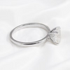 A silver-toned solitaire ring with a large clear triangular gemstone, displayed on a soft white fabric background.