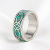 A silver band ring featuring a polished inlay of turquoise and green opal with a Celtic knot pattern cut out of the silver, set against a clean white background.