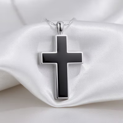 A silver cross pendant with a glossy black inlay, hanging from a silver chain and displayed on draped white satin fabric.