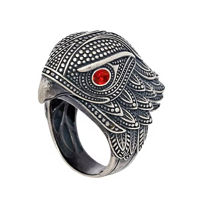 An ornate silver-toned ring shaped like an eagle or bird head, featuring intricate engraved patterns and a single red gemstone in the eye, shown on a plain white background.