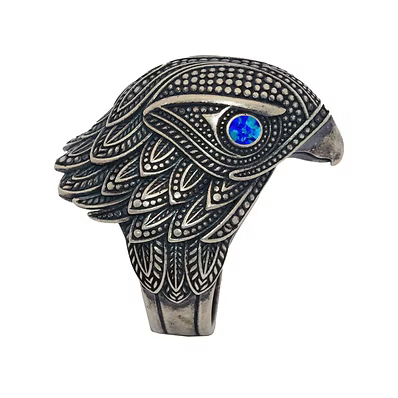 An ornate silver-toned ring shaped like an eagle head, featuring intricate filigree detailing and a round blue opal inlay for the eye, shown on a plain white background.