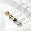 Four silver heart-shaped pendant necklaces arranged diagonally on a white satin fabric background, each featuring a different heart color: gold, gold with clear stones, black with clear stones, and silver with clear stones.