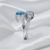 A polished silver ring featuring two oval-cut light blue opal gemstones, displayed on a draped white satin fabric background.