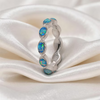 A silver ring featuring a multitude of oval-cut blue opal gemstones, displayed on draped white satin fabric.