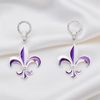 A pair of silver-tone fleur-de-lis drop earrings with purple and white enamel detailing, displayed on a draped white satin fabric background.