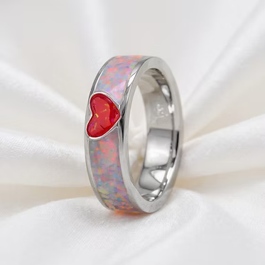 A polished silver ring featuring a vibrant red heart-shaped opal inlay on a white draped fabric background.