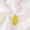A silver chain necklace with a rectangular yellow pendant, displayed on draped white satin fabric.