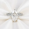 A silver ring with a large marquise-cut clear gemstone in a prong setting, displayed on a soft white satin fabric background.