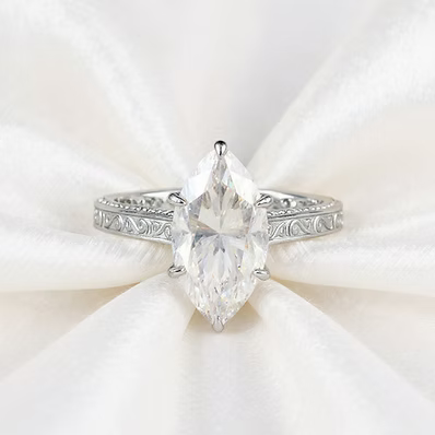 A silver ring with a large marquise-cut clear gemstone in a prong setting, displayed on a soft white satin fabric background.