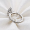 A silver ring with an engraved band and a large clear gemstone, displayed on a textured white fabric background.