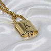 A gold padlock pendant necklace with a monogram letter 'K' on the front, resting on a white satin fabric background.