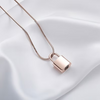 A rose gold padlock pendant necklace on a delicate chain, displayed on a draped white satin fabric background.