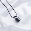 A black padlock pendant necklace on a black cord, displayed on a draped white satin fabric background.