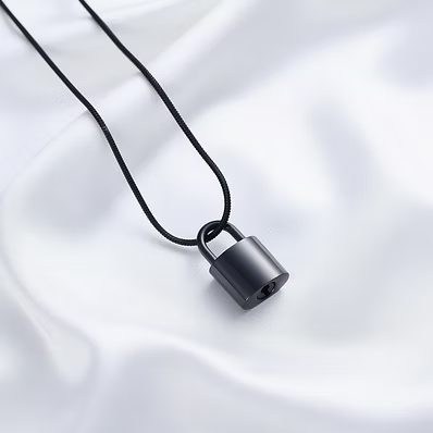 A black padlock pendant necklace on a black cord, displayed on a draped white satin fabric background.