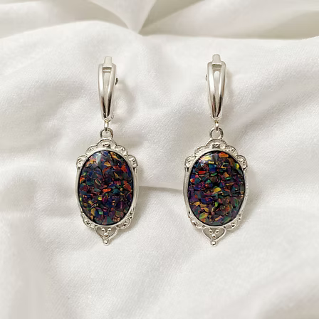 A pair of silver leverback earrings with oval iridescent opal-like stones, displayed on a soft white fabric background.