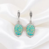 A pair of silver drop earrings with oval opal gemstones, displayed on a draped white satin fabric background.