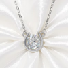 A silver horseshoe pendant necklace with a large clear faceted gemstone, displayed on a white satin fabric background.