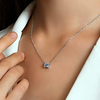 A close-up of a delicate silver chain necklace with a small square-cut clear gemstone pendant, worn on a model's neck with a white collared shirt visible.