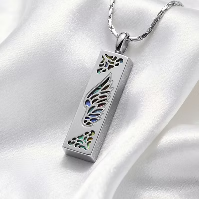 A silver rectangular pendant necklace with a wing design and iridescent inlay, resting on white satin fabric.