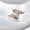 A silver leaf-shaped ring with beige inlay details, displayed on a soft white satin fabric background.