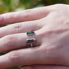 A close-up of a hand wearing two silver rings. The top ring has a small rectangular green stone, and the bottom ring is an open band with the word 'DAD' engraved on a polished silver bar.