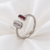 A silver-toned open ring band featuring a polished rectangular silver charm engraved with 'WOW' and a smaller top bar with a colorful, iridescent inlay, displayed on a soft white fabric background.