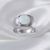 A silver-toned signet ring featuring a round, milky white opal gemstone, displayed on draped white satin fabric.