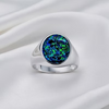 A silver signet ring featuring a round bezel-set iridescent opal stone with vibrant blue, green, and black play-of-color, displayed on a draped white satin fabric background.