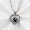 A silver heart-shaped pendant necklace with a paw print cutout, displayed on a white satin fabric background.
