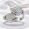 A silver ring featuring two overlapping teardrop-shaped opal stones with iridescent multicolor play-of-color, set in polished silver bezel settings on a white satin background.