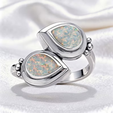 A silver ring featuring two overlapping teardrop-shaped opal stones with iridescent multicolor play-of-color, set in polished silver bezel settings on a white satin background.